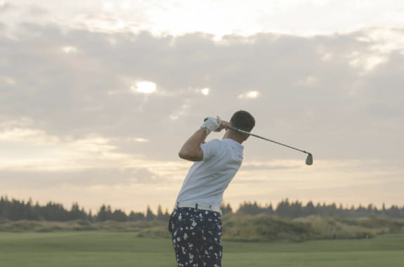 Male golfer in mid-swing on a golf course at sunset, symbolizing elite athletic performance and global ambition – banner image for Hogan Lovells and GSE Worldwide case study