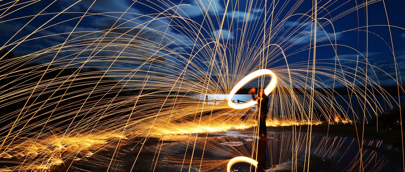 A long exposure of steel wool spinning on a with sparks reflected in a lake