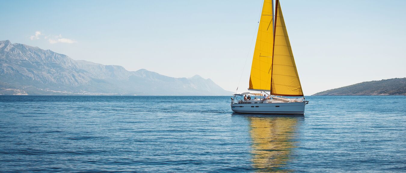 Sailboat on calm waters with mountain range in background.