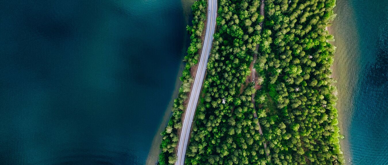 Aerial view of road between green summer forest and blue lake in Finland