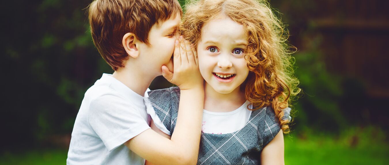 Boy whispering in girls ear.