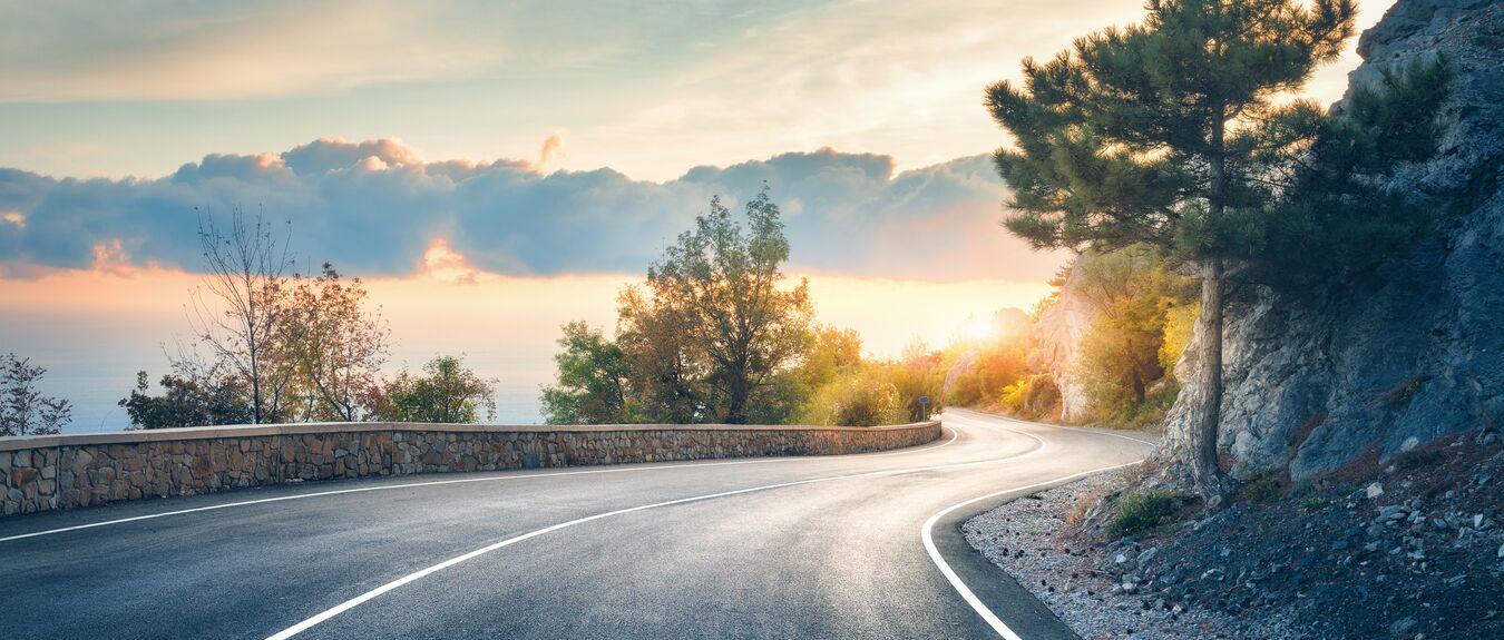 Mountain road. Landscape with rocks, sunny sky with clouds and beautiful asphalt road in the evening in summer. Vintage toning. Travel background. Highway in mountains. Transportation